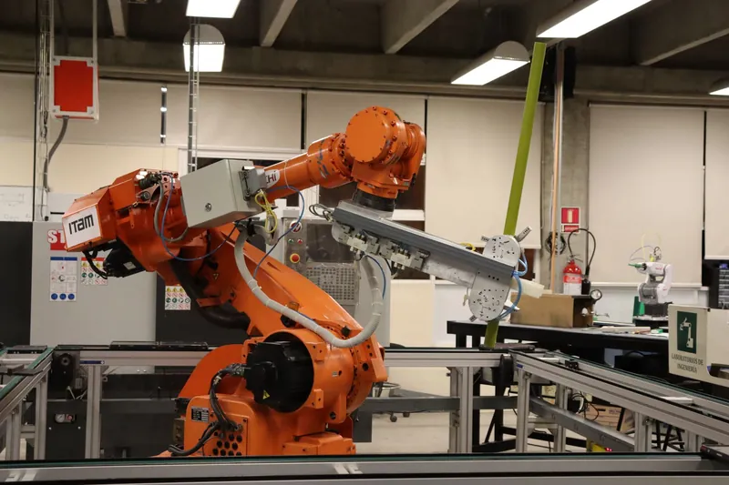 Oranger Industrieroboter mit langer Greiferleiste über einem Fördersegment in einer Werkhalle